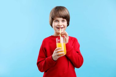 Açık mavi arka planda bir bardak taze portakal suyu olan çocuk.