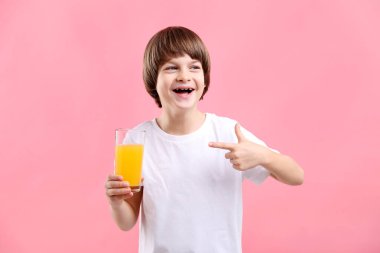Çocuk pembe arka planda taze portakal suyu bardağını işaret ediyor.