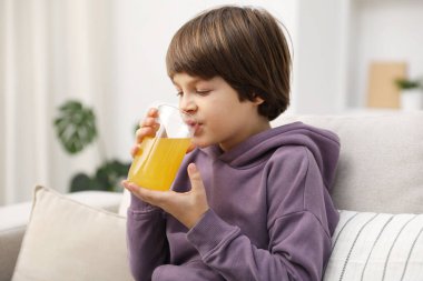 Çocuk evdeki kanepede taze portakal suyu içiyor.