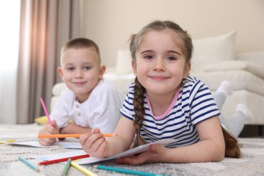 Evde yerde kalemlerle resim yapan çocuklar, seçici bir odak noktası.