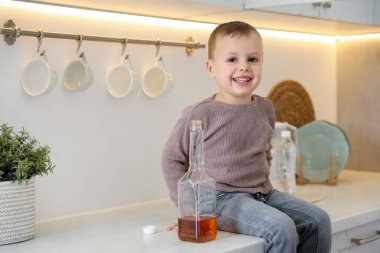 Evde çocuk güvenliği. Elinde alkol şişesi olan küçük çocuk mutfaktaki tezgahta oturuyor, mesaj atmak için yer var.