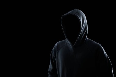 Anonymous man in hood on black background. Criminal concept