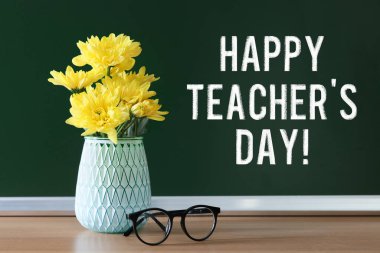 Öğretmenler Günün kutlu olsun! Yeşil karatahtanın yanındaki masada çiçek ve gözlüklü vazo.