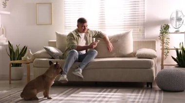 Akıllı telefonlu genç adam evdeki şirin köpeğin yanındaki kanepede dinleniyor.