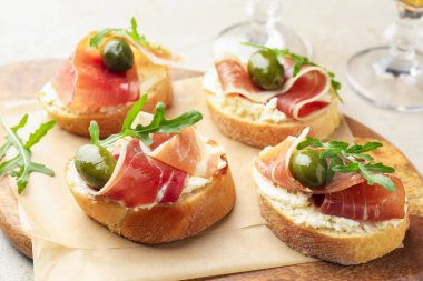 Krem peynirli nefis bruschettalar, prosciutto, yeşil zeytin ve roka masada, yakın plan.