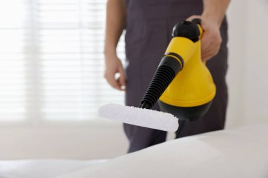 Haşere kontrol işçisi yatağı temizliyor, kapalı alanda buharlı temizleyiciyle, yakın plan. Metin için boşluk