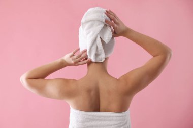 Pembe arka planda havluya sarılı güzel bir kadın.