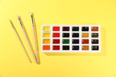 Sarı zemin üzerinde suluboya palet ve fırçalar, düz yatıyordu