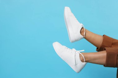 Açık mavi arka planda şık beyaz ayakkabılar giyen bir kadın, yakın plan. Metin için boşluk