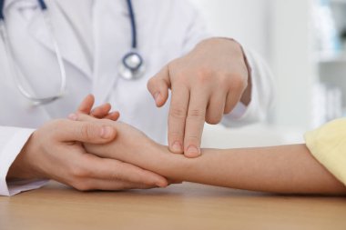 Doktor, klinikteki masada parmaklarıyla kadının nabzını kontrol ediyor.