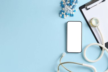 Sağlığınıza. Akıllı telefon, steteskop, açık mavi arka planda pano hapları, düz yatak. Metin için boşluk