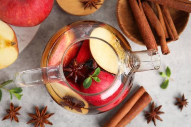 Aromatic fruit tea in glass teapot, apples, mint and spices on grey table, flat lay