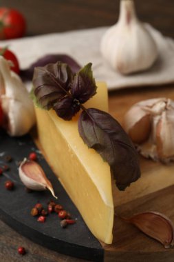 Süt ürünü. Bir parça peynir, fesleğen, biber ve sarımsak ahşap masada, yakın plan.