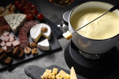 Erimiş peynirle fondü tenceresi (caquelon) ve siyah masada atıştırmalıklar, yakın plan.