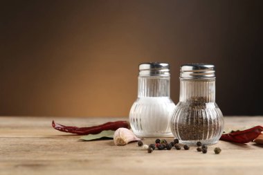 Kahverengi arka planda, ahşap masada baharatlı tuzluk ve biberlikler, yakın plan. Metin için boşluk