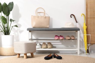 Farklı ayakkabılar, aksesuarlar ve beyaz duvarın yanındaki ev bitkilerinden oluşan ayakkabı deposu.