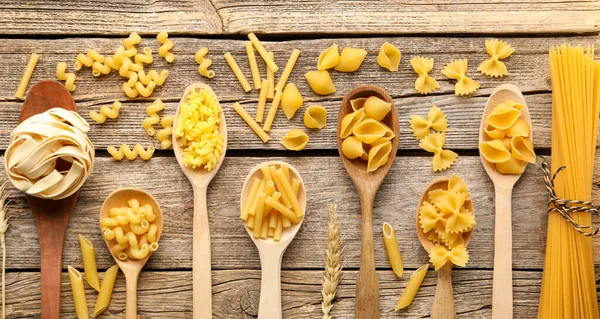 Farklı türde çiğ makarnalar, kaşık ve çiviler, tahta masa, düz yatış
