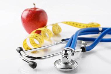 Olgun elma, steteskop ve beyaz masadaki mezura, yakın plan.