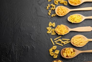 Siyah masadaki tahta kaşıklarda farklı türde çiğ makarna, düz yerde. Metin için boşluk