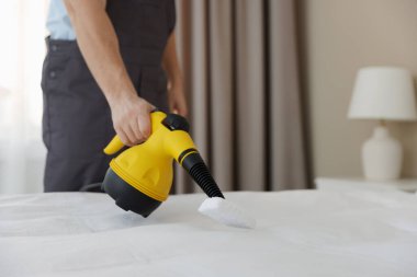 Haşere kontrol işçisi yatağı temizliyor, kapalı alanda buharlı temizleyiciyle, yakın plan. Metin için boşluk