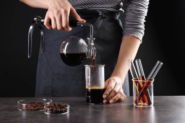 Gri masadaki cam şişeye kahve dolduran kadın, yakın plan.