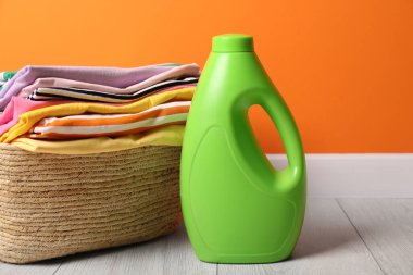 Çamaşır sepetinin içinde kıyafetler ve bir şişe deterjan var. Kapalı turuncu duvarın yanında, yakın plan.