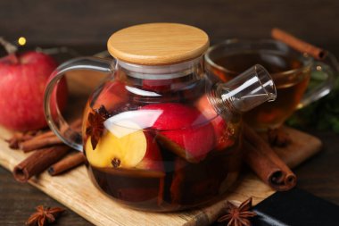 Aromatik meyve çayı cam çaydanlıkta, fincan, elma ve baharatlar ahşap masada, yakın plan.