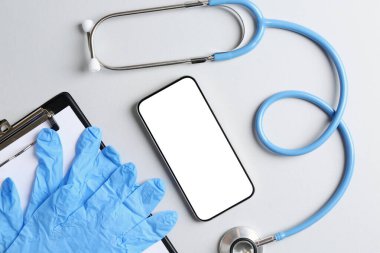 Sağlığınıza. Akıllı telefon, steteskop, tıbbi eldiven ve arka planda pano, düz uzanma