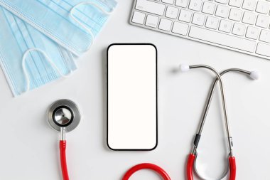 Sağlığınıza. Akıllı telefon, klavye, steteskop ve sağlık maskeleri ışık masasında.