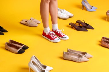 Sarı arka planda farklı ayakkabıları olan kadın, yakın plan.