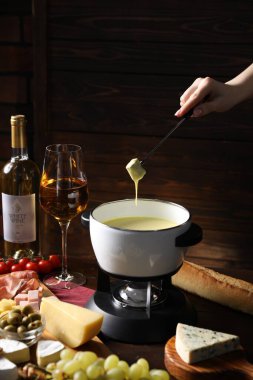 Kadın, ahşap masada erimiş peynirle fondü kabına (caquelon) bir parça ekmek daldırıyor.