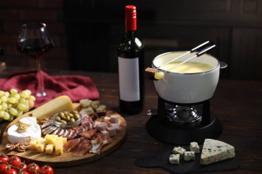 Nefis eritilmiş peynir fondü kabında, abur cuburlar ve bir şişe şarap ahşap masada, karanlık arka planda, yakın planda