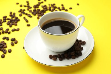 Aromatik kahve çekirdekleri ve fincanlar sarı arka planda, yakın plan.