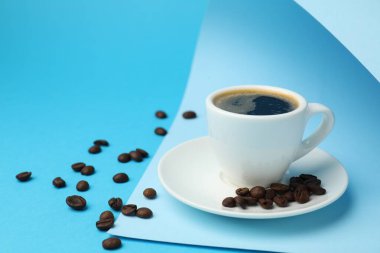 Kahvenin fincanda tazelenmesi, açık mavi arka planda fasulye ve kağıt yaprağı, yakın plan