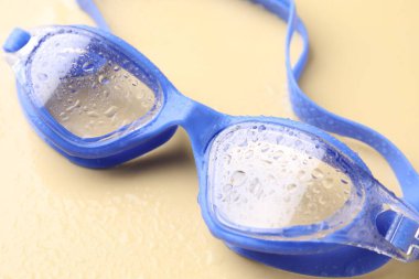 Sarı arka planda su damlaları olan yüzme gözlükleri, yakın plan