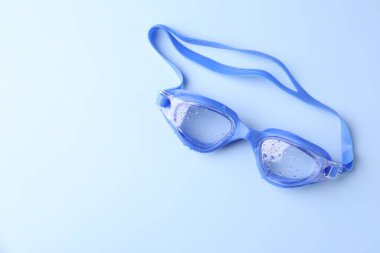 Açık mavi arka planda su damlaları olan yüzme gözlükleri, üst manzara. Metin için boşluk