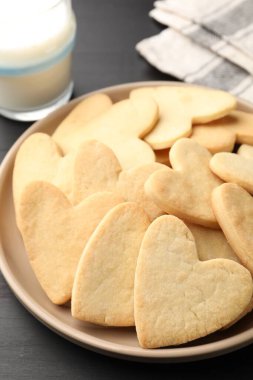 Lezzetli kalp şeklinde kurabiyeler ve süt karanlık masada, yakın plan.