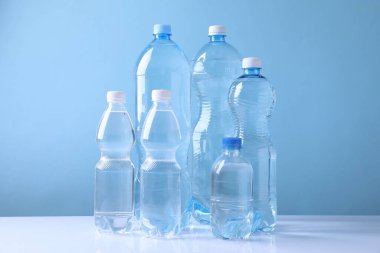 Açık mavi arka planda beyaz masada farklı boyutlarda su şişeleri