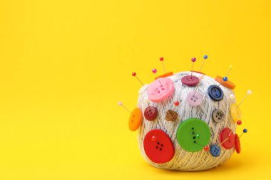 Sarı arka planda iğneler ve düğmeler olan iplik yumağı, yakın plan. Metin için boşluk