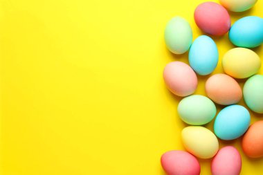 Many painted Easter eggs on yellow background, flat lay. Space for text