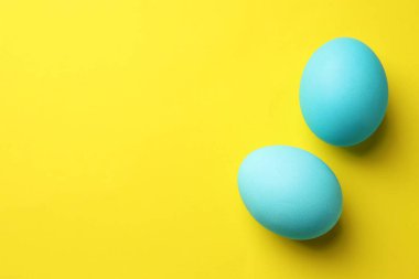 Painted Easter eggs on yellow background, flat lay. Space for text