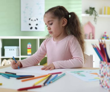 Masada pastel boyayla resim çizen sevimli küçük kız.