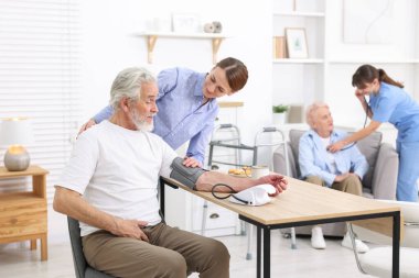 Bakıcı evde yaşlı adamın kan basıncını ölçüyor.