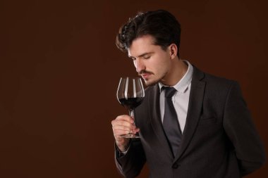 Profesyonel şarap garsonu kahverengi arka planda kırmızı şarap tadıyor. Metin için boşluk