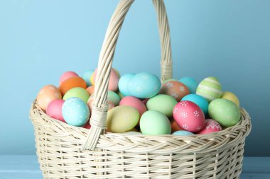 Güzel dekore edilmiş Paskalya yumurtaları hasır sepette açık mavi ahşap masada, yakın plan.