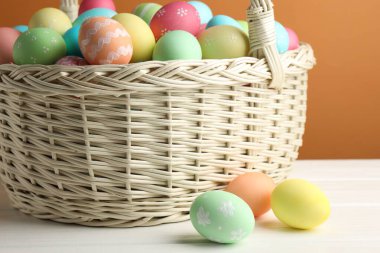 Güzel dekore edilmiş Paskalya yumurtaları hasır sepetin içinde beyaz ahşap masada kahverengi arka planda, yakın planda.