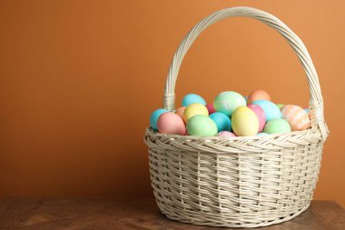 Güzel dekore edilmiş Paskalya yumurtaları hasır sepetin içinde, ahşap masada kahverengi arka planda, metin için yer var.
