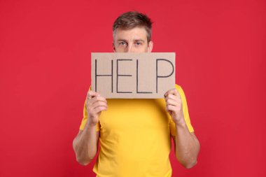 Mutsuz adam kırmızı arka planda kelime yazılı karton tabela tutuyor.