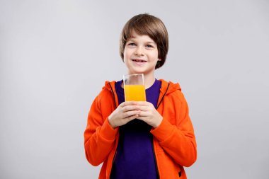 Açık gri arka planda bir bardak taze portakal suyu olan çocuk.