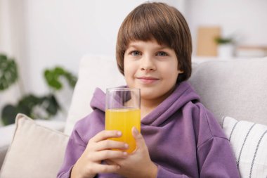 Evdeki kanepede bir bardak taze portakal suyu olan çocuk. Metin için boşluk